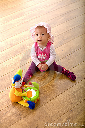 Baby Girl  9 Months  Sitting On Hardwood Floor Together With A Toy    
