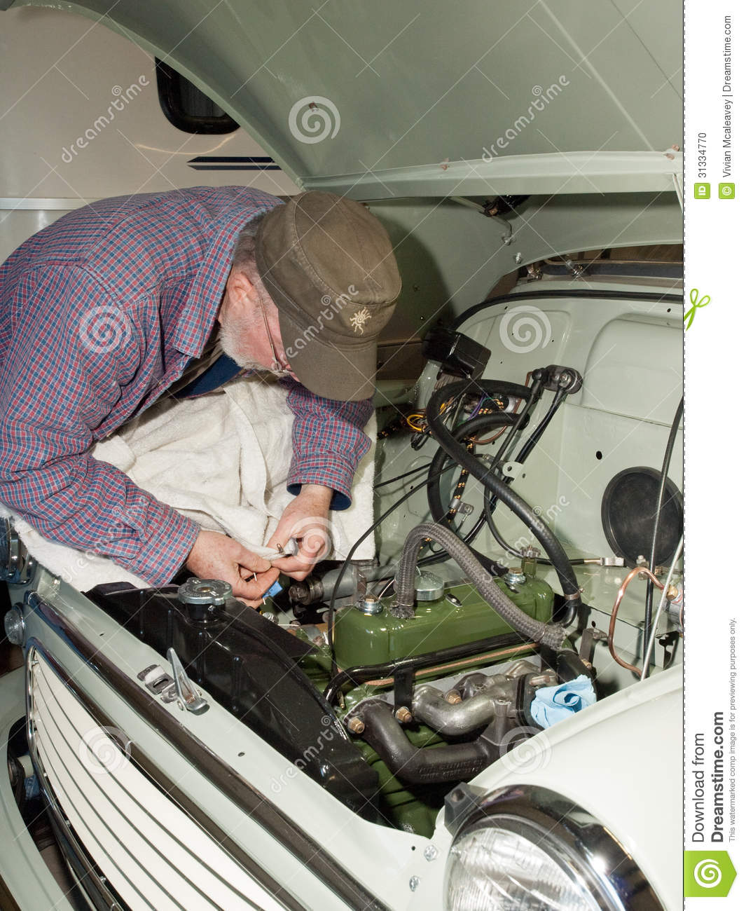 Senior Man Making Adjustments To The Engine Of A Vintage Car He Is