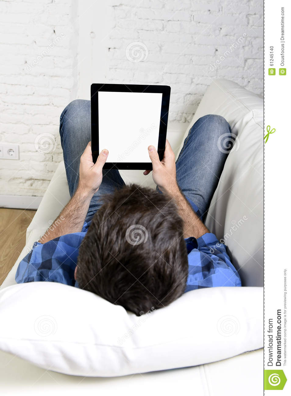 Man Lying On Home Couch Using Digital Tablet Pad In Portable Internet