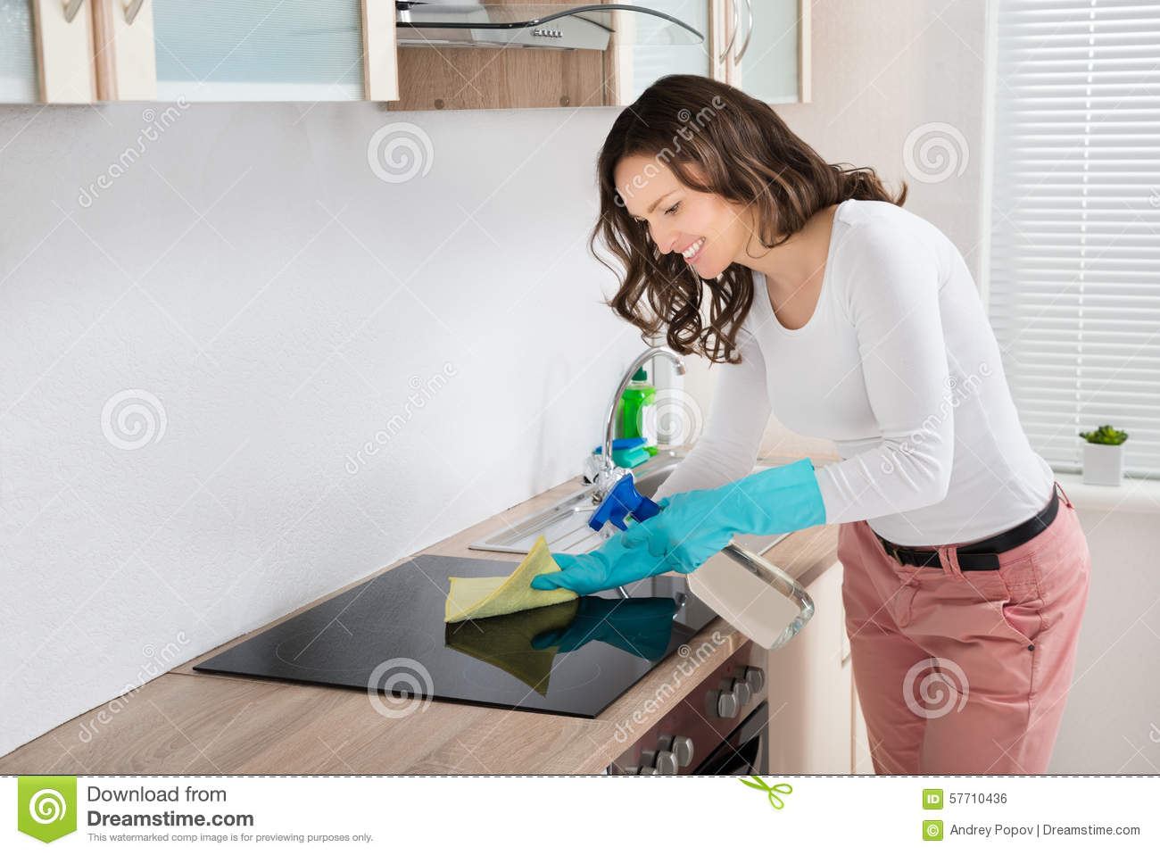 Young Woman Smiling While Cleaning Induction Hob On Countertop At Home