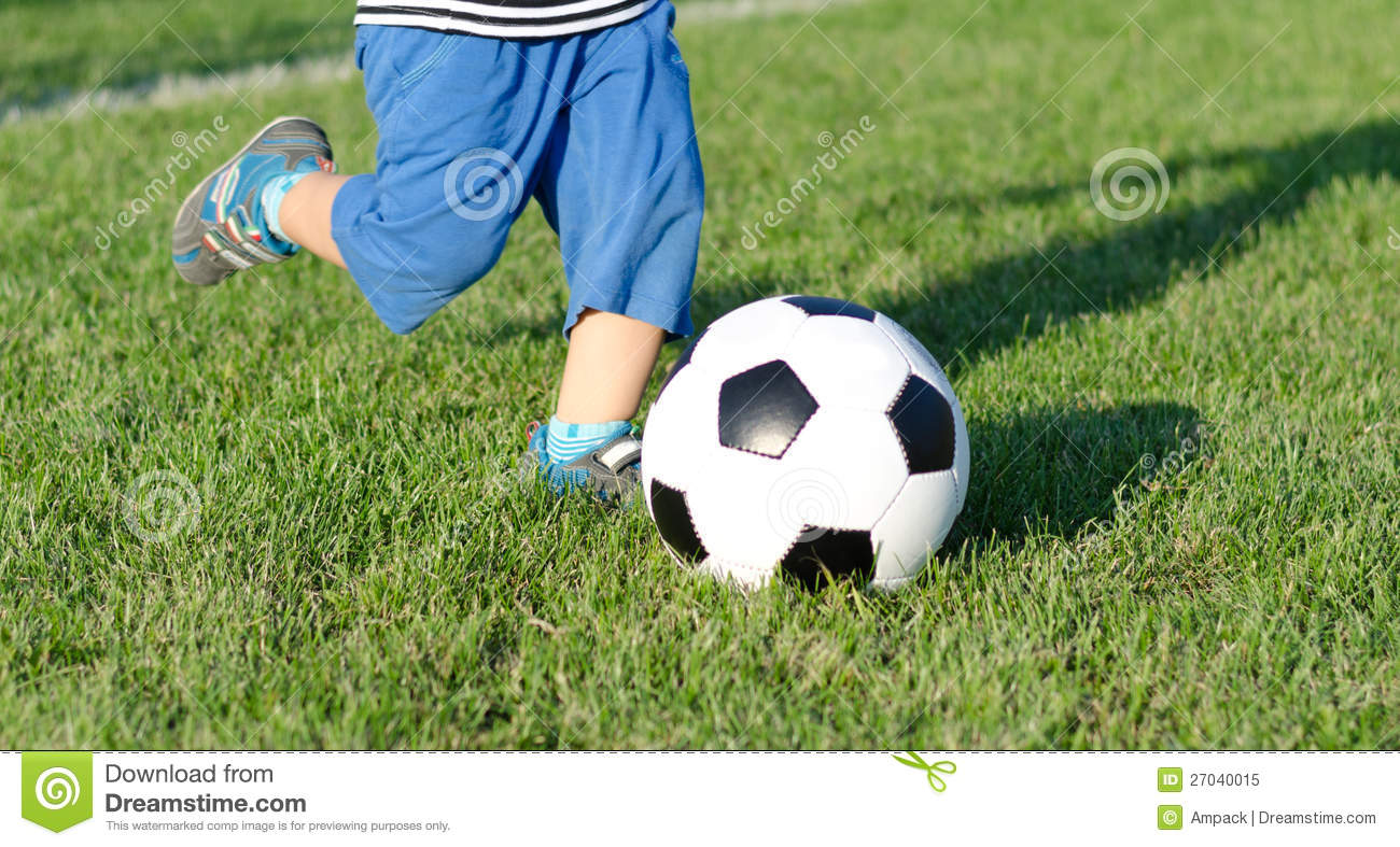 The Legs Of A Little Boy Kicking A Soccer Ball On A Green Sportsfield