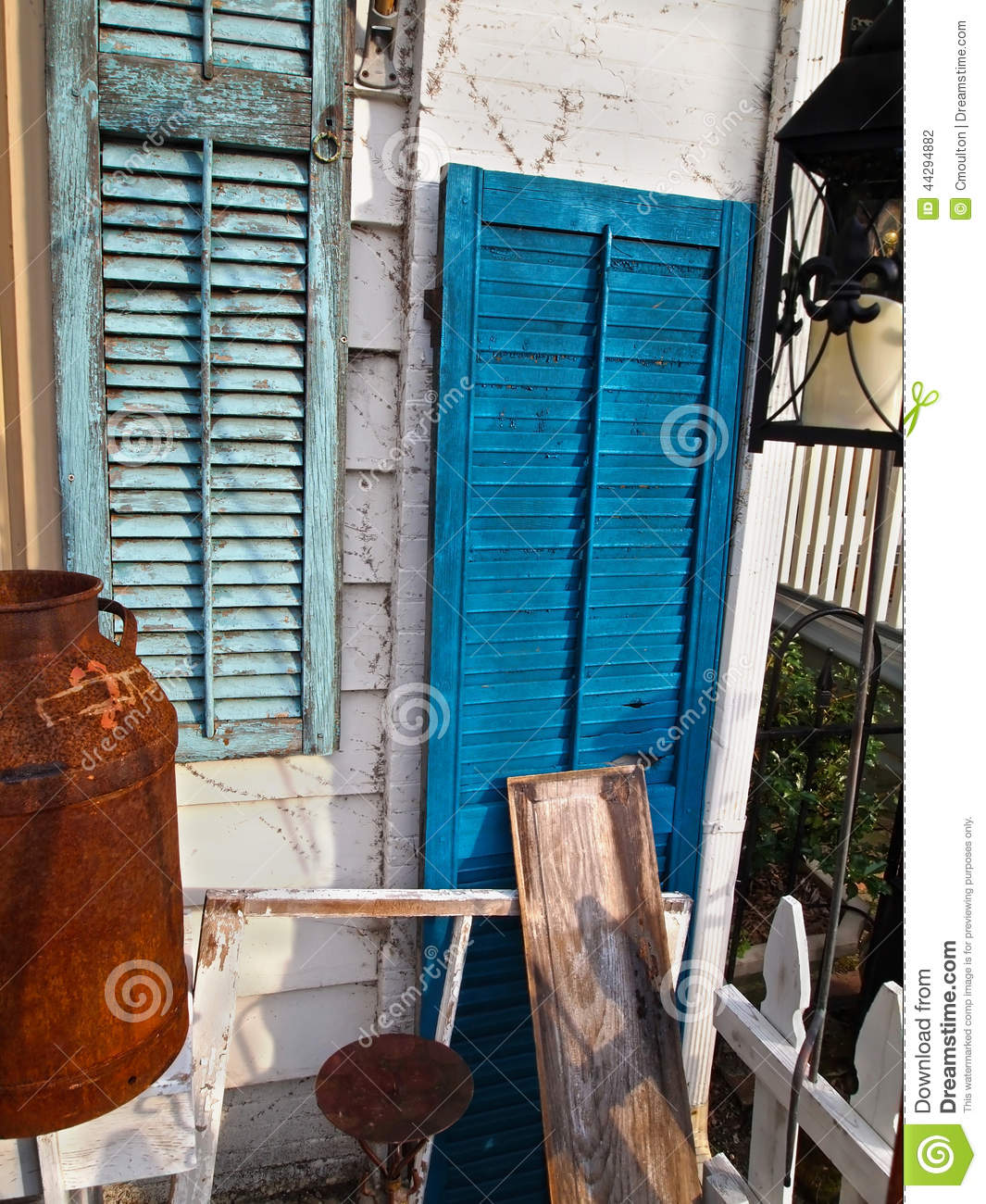 Shutters With Peeling Paint On An Aging Porch Full Of Vintage Items