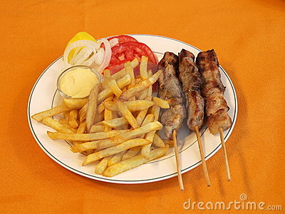 Greek Souvlaki With French Fries And Garnishments On A White Plate