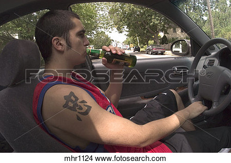 Male Teen With A Tattoo On His Arm Drinking A Beer While Driving A Car    
