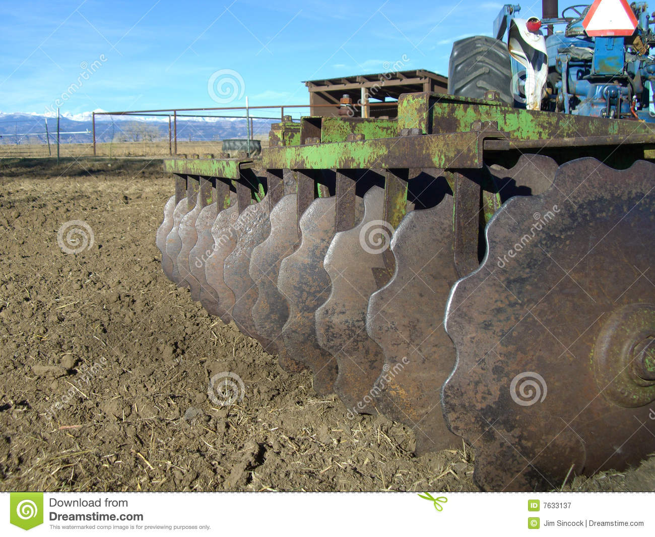 Disk Harrow And Tractor In Farm Field With Mountains In Background