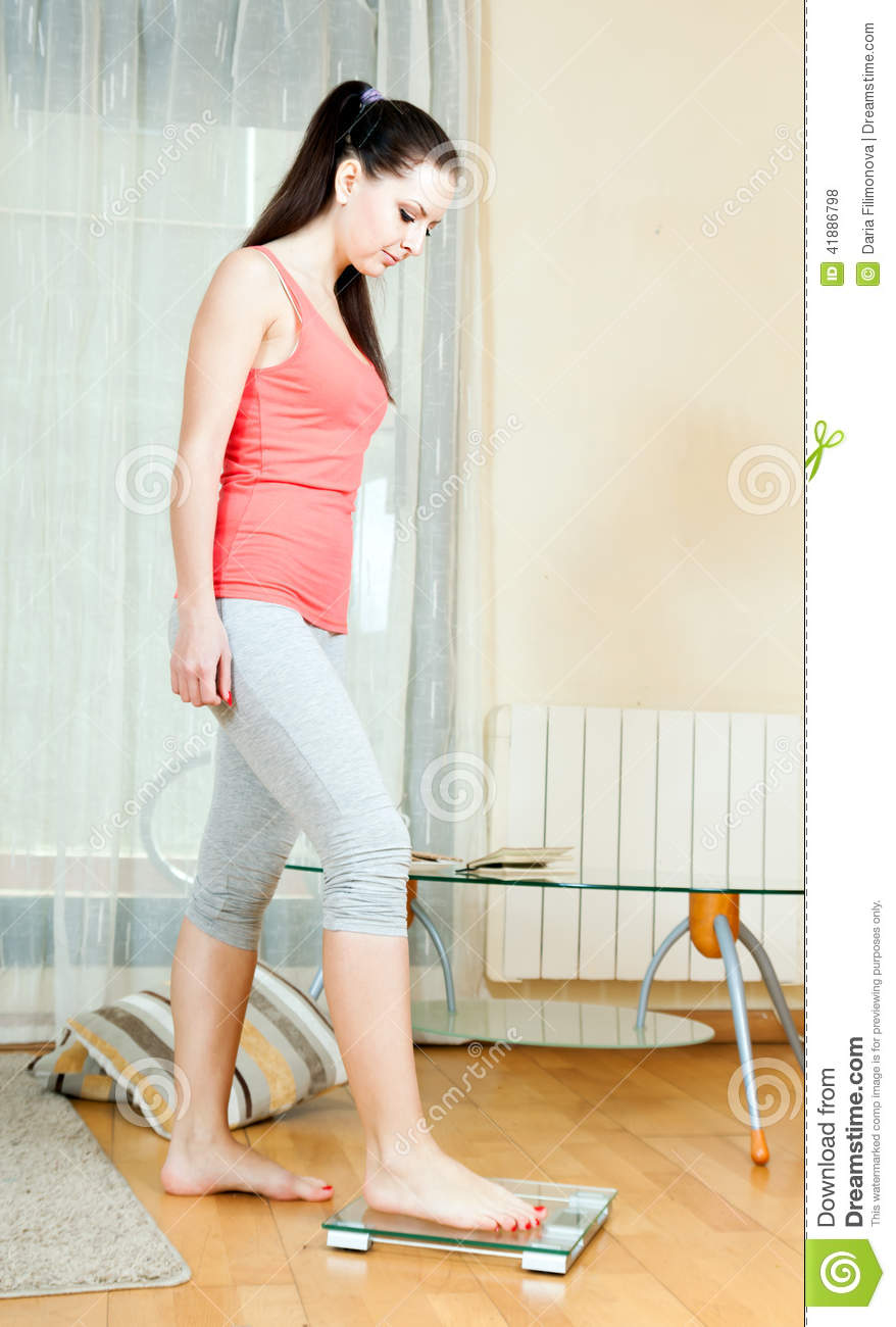 Girl Weighing Herself On Bathroom Scale At Home Interior
