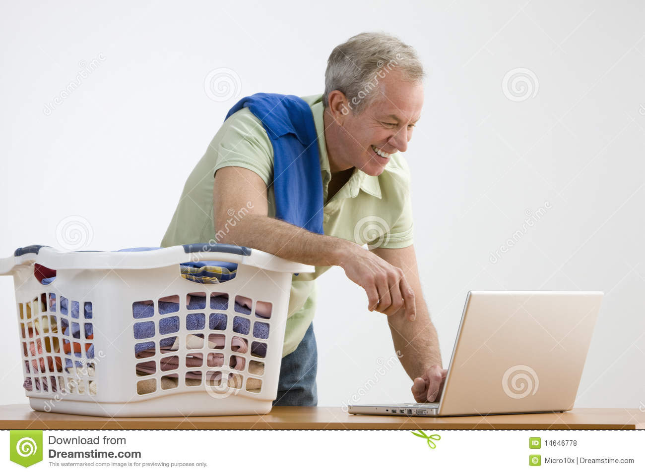 Man Is Working On A Laptop While He Folds Laundry  He Is Smiling And    