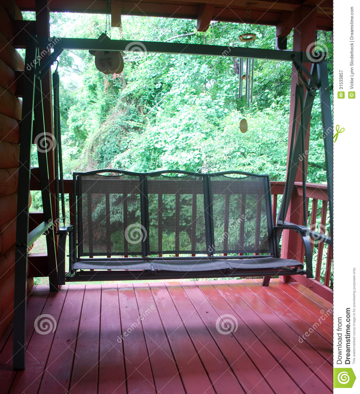 Green Porch Swing Located On The Wooden Back Deck Of A Log Home In