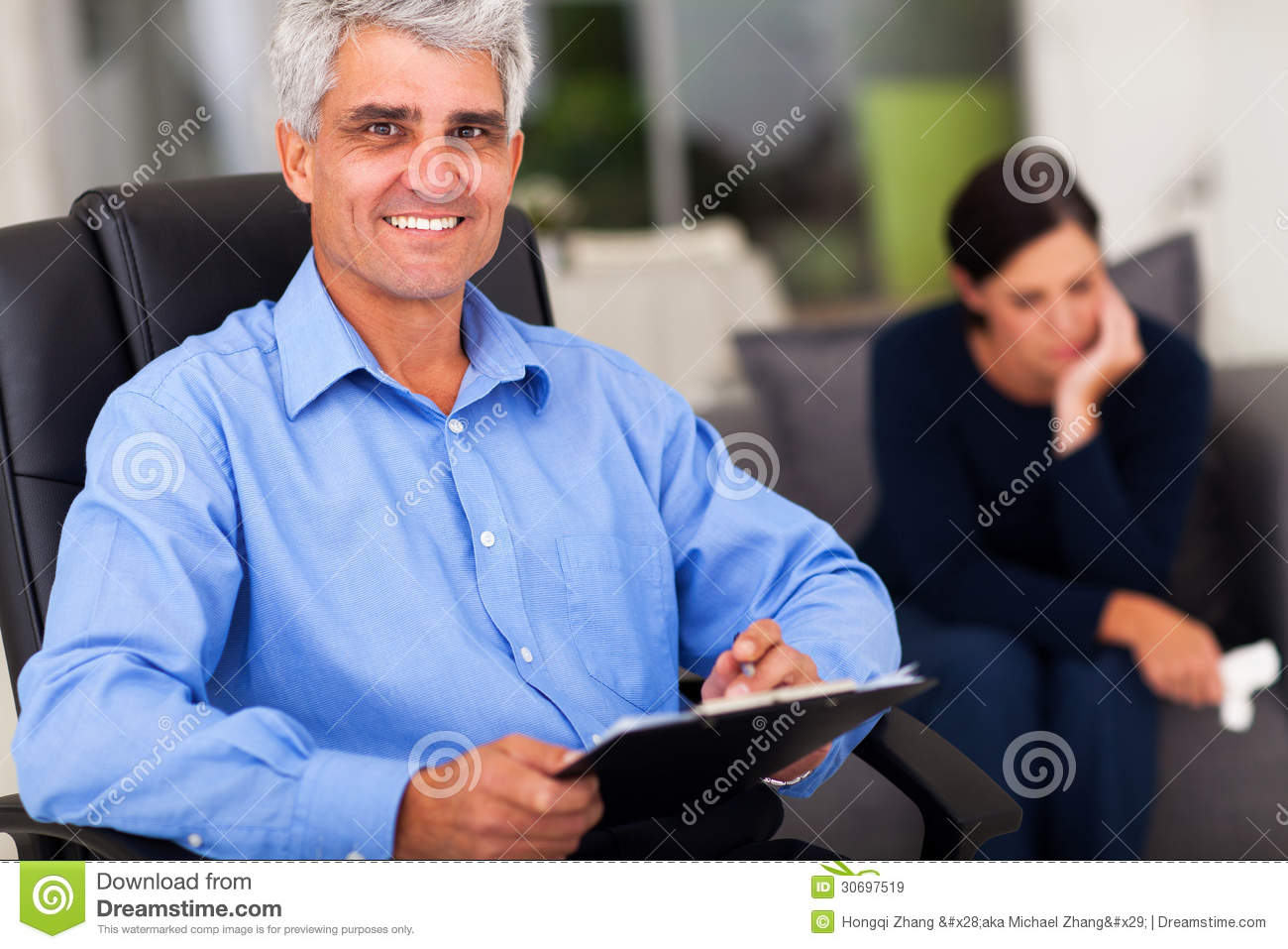 Portrait Of Middle Aged Male Psychologist In Office With Patient In