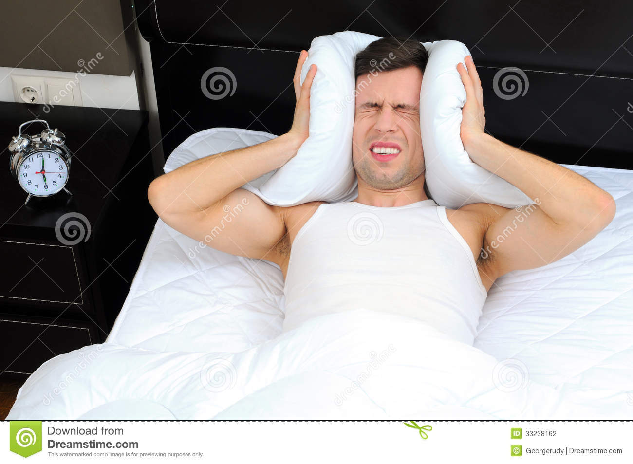Young Male Adult Stressed By His Alarm Clock With His Head Under The