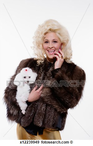 Young Blonde Woman In Fur Coat Holding White Poodle And Using Mobile