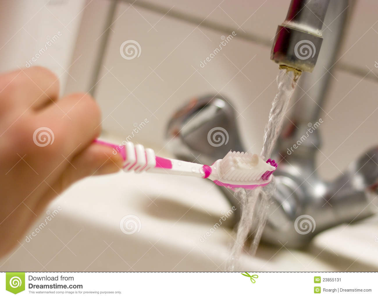 Hand Holding A Pink Toothbrush With Toothpaste On Top Under A Running
