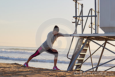 Woman Stretching Leg Muscle Before Early Morning Run Workout On Beach 