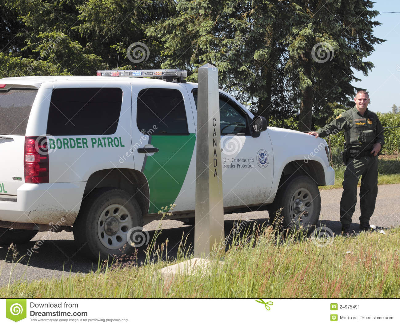Border Patrol Officer Stands Beside His Vehicle Parked In Front Of A    
