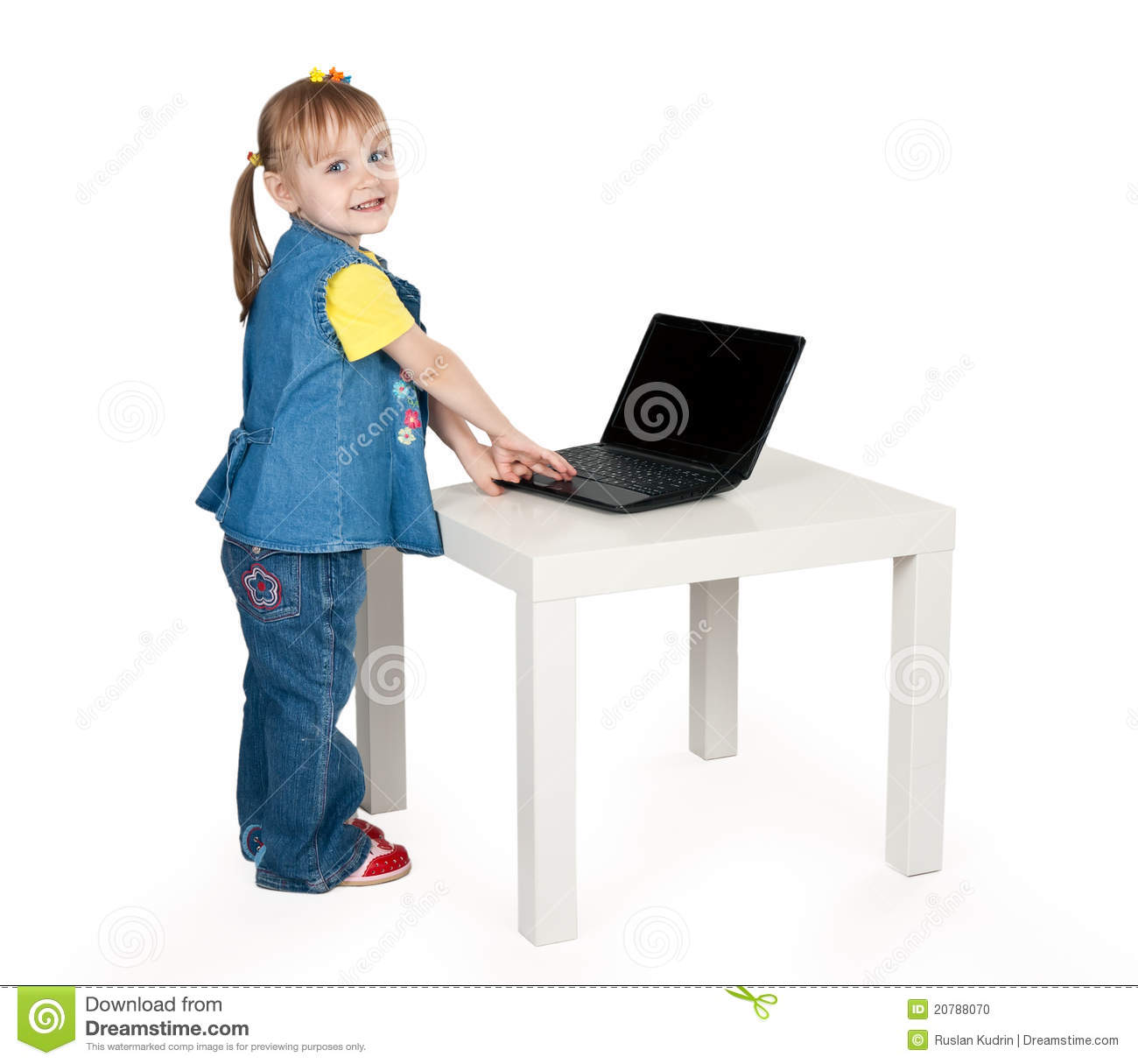 Little Girl In Blue Jeans Standing At A Table With A Laptop In The