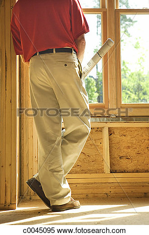 Man Holding Plans Looking Out Window Inside A House Under Construction