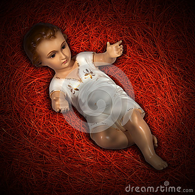 Baby Jesus Figurine Lying In Manger On Red Straw Background With