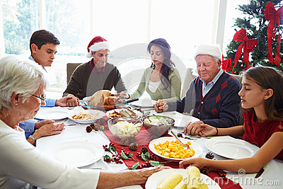 Multi Generation Family Praying Before Christmas Meal Sitting Around    
