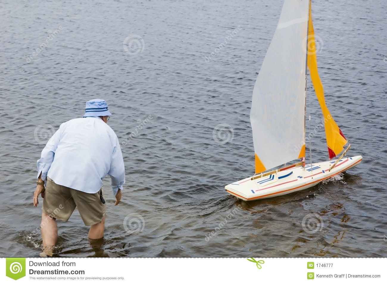 Radio Controlled Model Sailboat On Lake Being Launched By Senior    