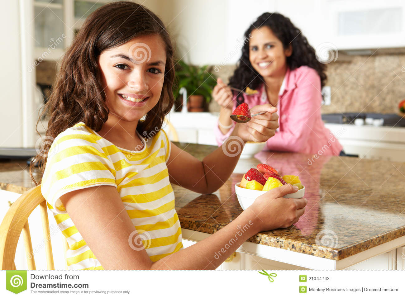 Mother And Daughter Eating Cereal And Fruit Together Smiling At Camera