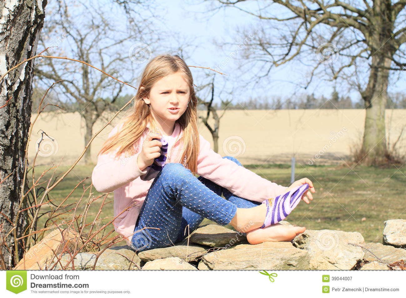 Pink Jacket Blue Pants Taking Off Socks While Sitting On Stone Wall