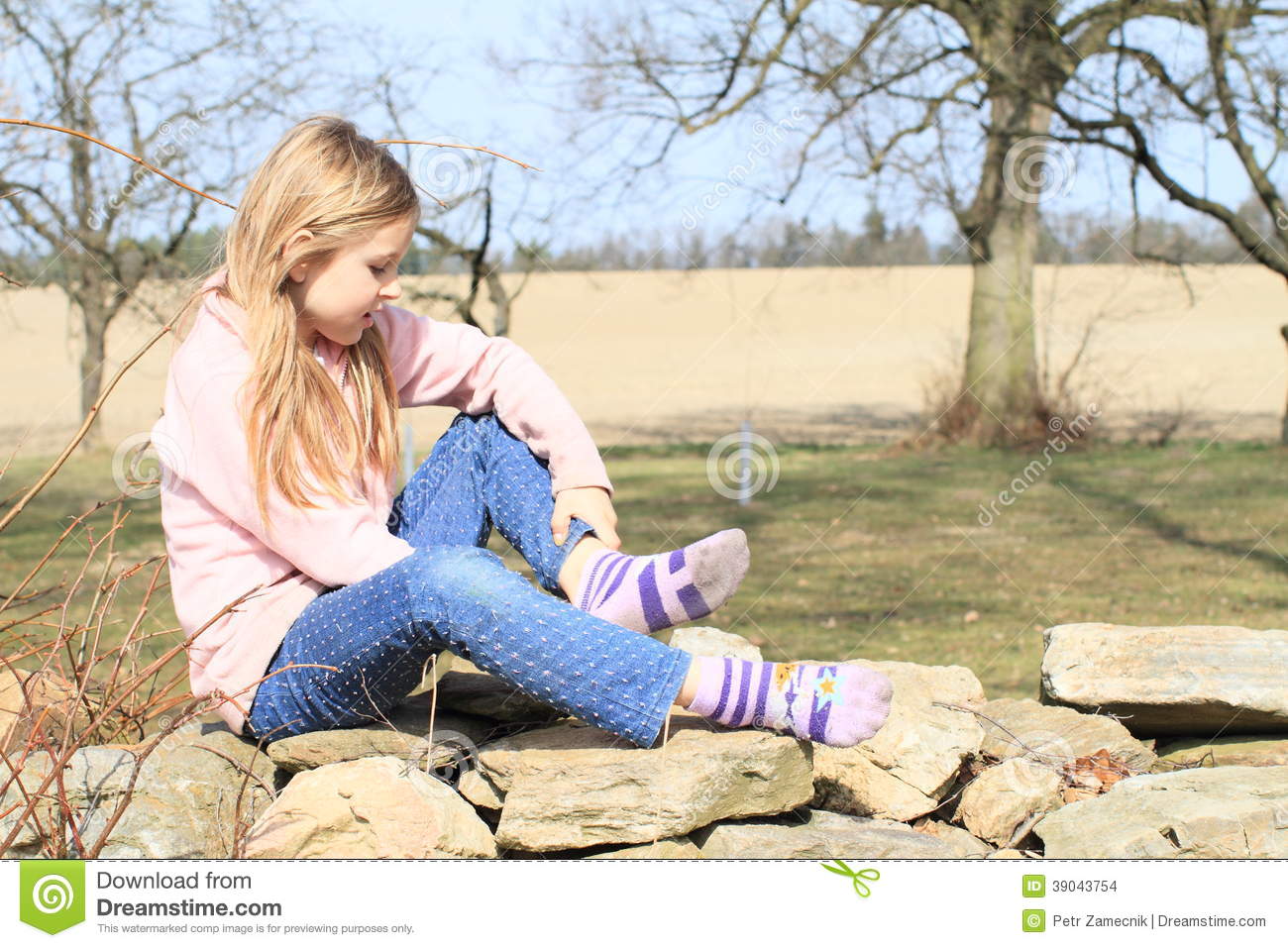 Pink Jacket Blue Pants Taking Off Socks While Sitting On Stone Wall