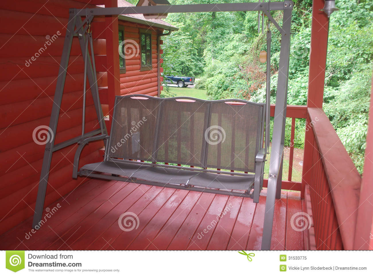 Green Porch Swing Located On The Wooden Back Deck Of A Log Home In    