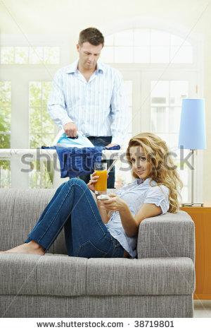 Happy Woman Sitting At Couch Watching Tv Man Ironing In The