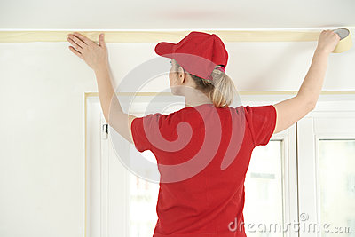 Woman Painter Worker Protecting Ceiling Moulding With Masking Tape