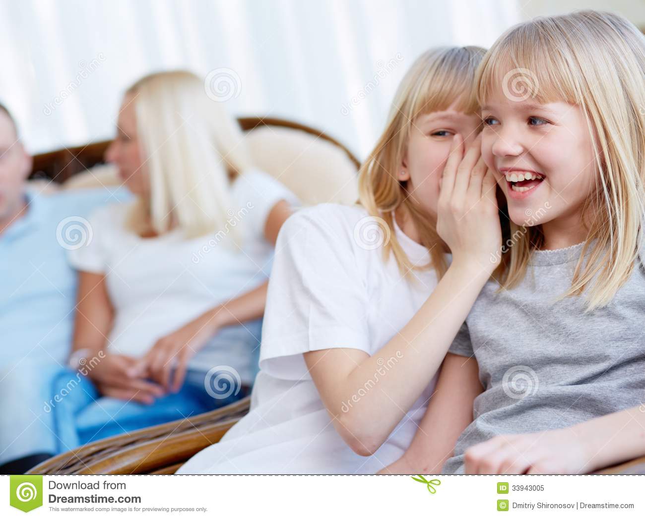 Portrait Of Happy Girl Laughing While Her Twin Sister Whispering    
