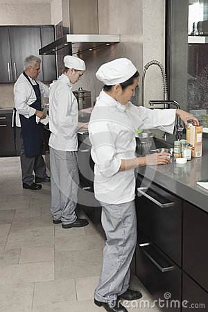 Three Chefs Working Together In Busy Commercial Kitchen 