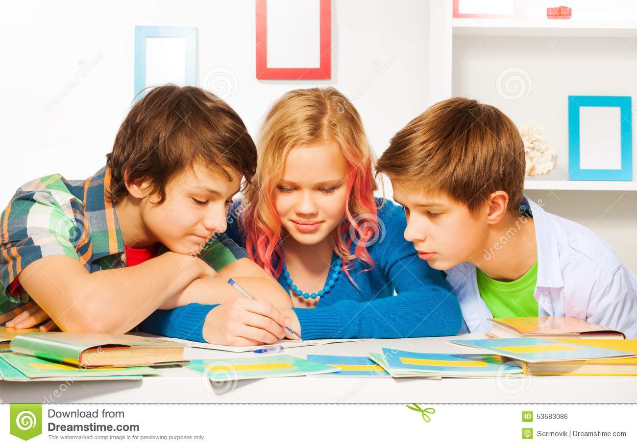 Three Cute Young Teens Do Homework And Write Together In Textbook