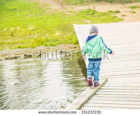 Child In Full Growth Is On The Edge Of A Wooden Pontoon Next To The