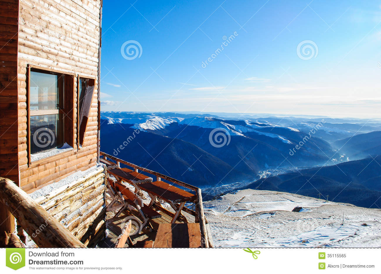 Wooden Cabin Facing The Snowy Peaks Of Mountains In The Cold Winter
