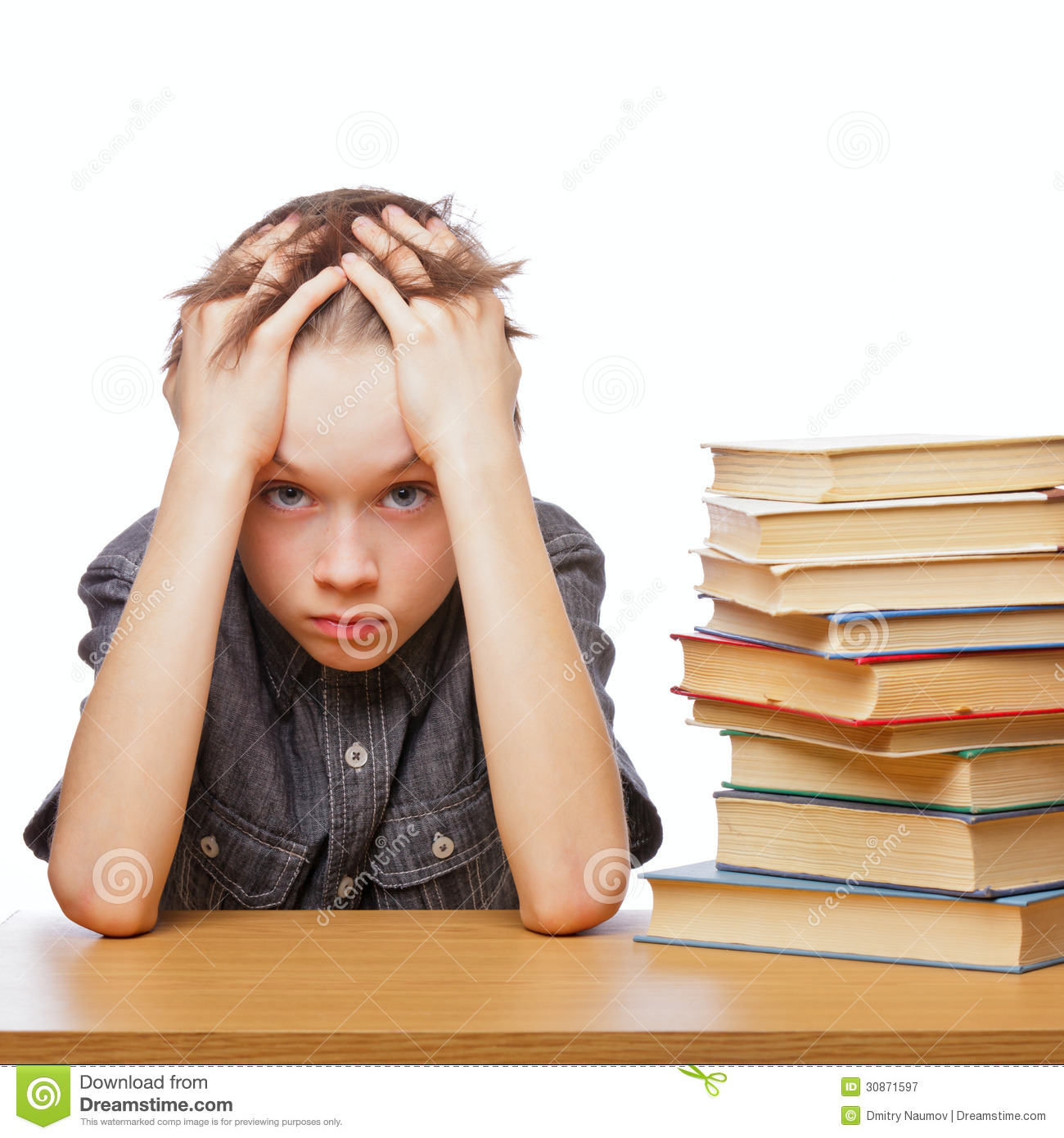 Portrait Of Upset Schoolboy Sitting At Desk With Books Holding His    