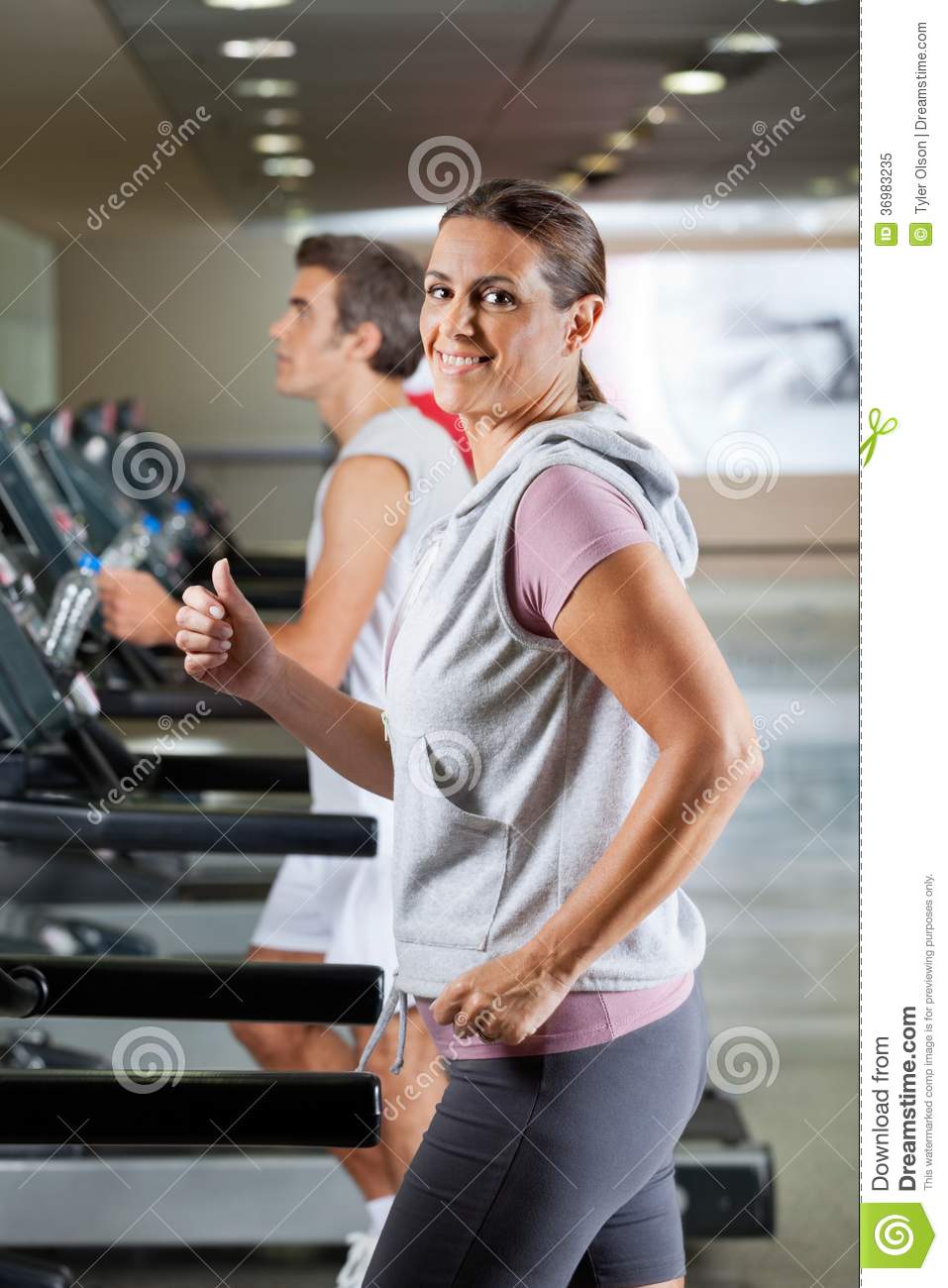 Side View Of Happy Mature Women And Men Running On Treadmill In Health    