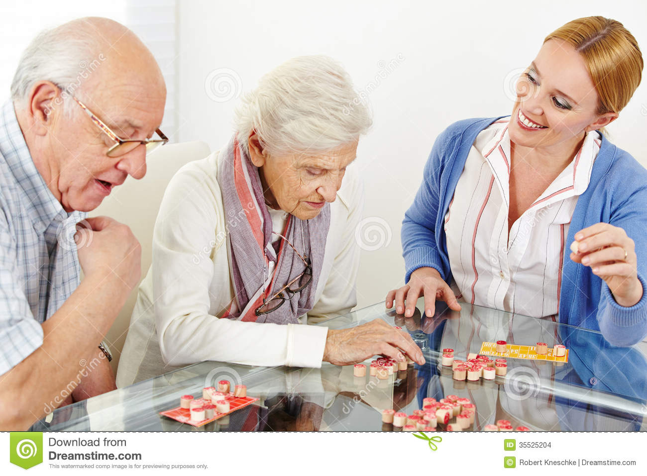 Senior Couple Playing Bingo With Eldercare Assistant In Nursing Home