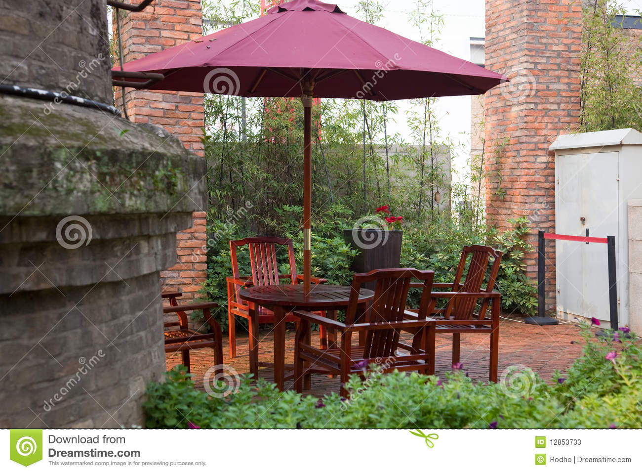 Summer Patio With Tables And Wooden Chairs Under Umbrella In Garden 