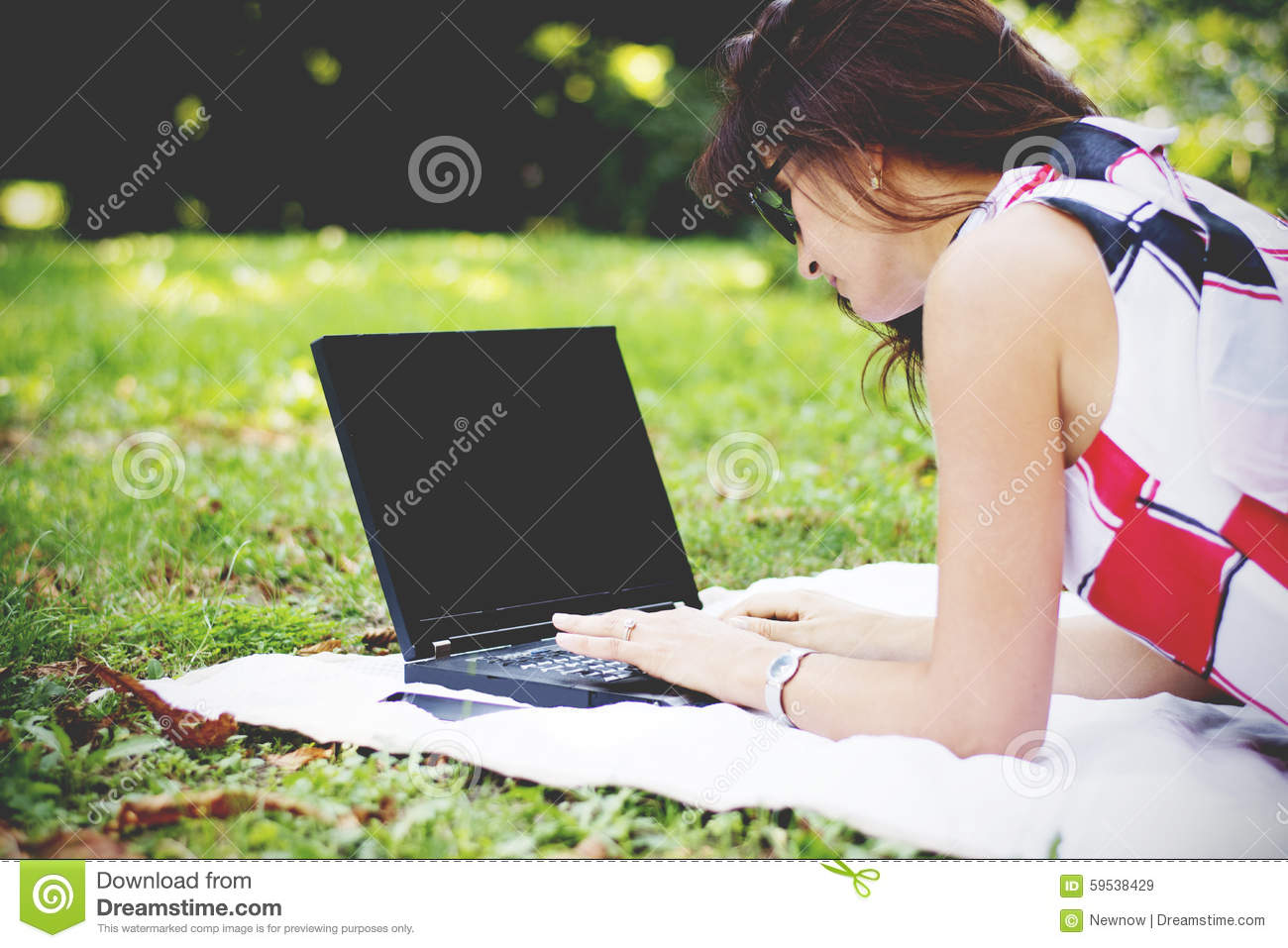 Young Brunette Woman In Park Using Laptop While Relaxing On A Blanket