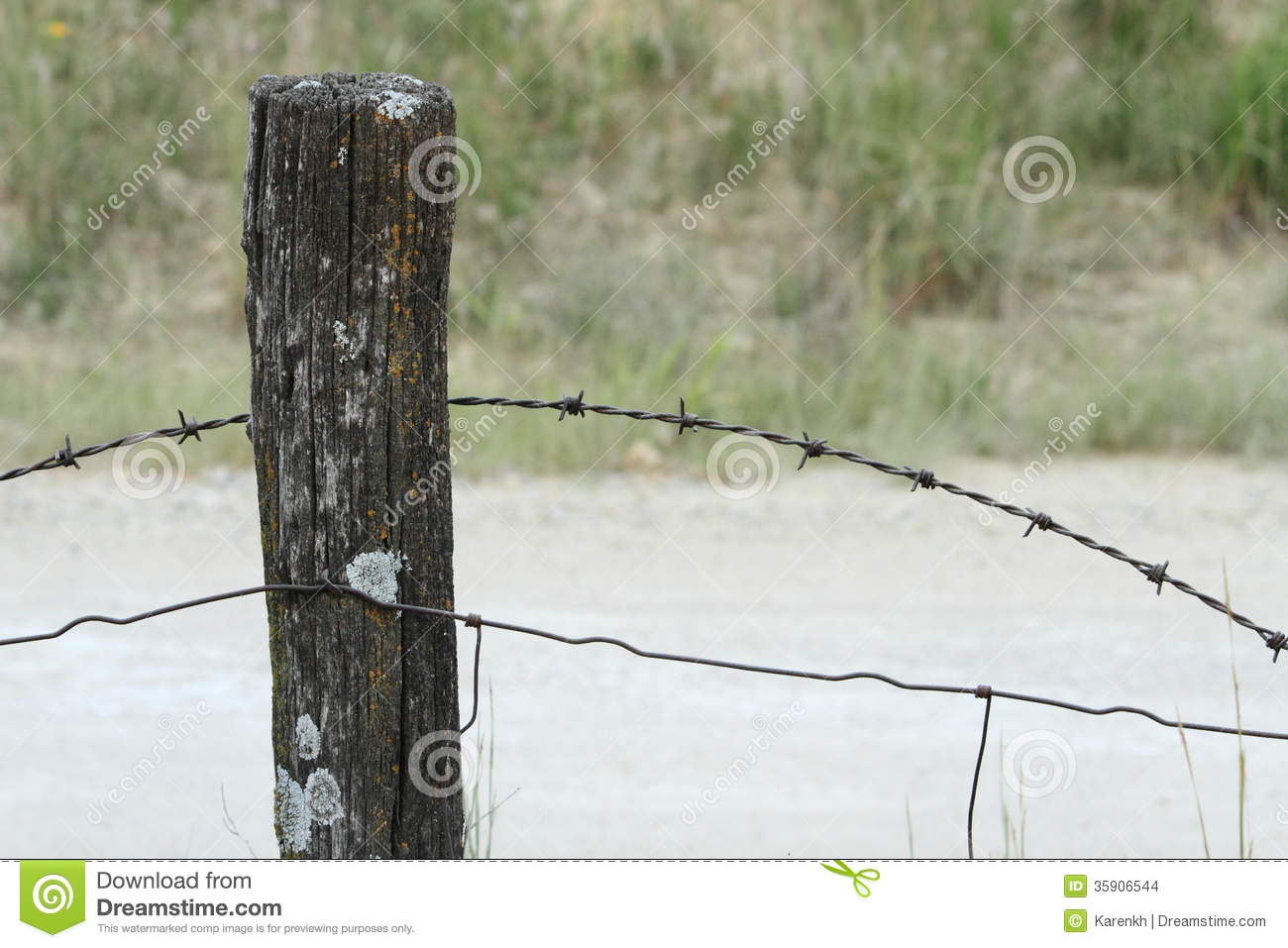 An Old Log Fence Post With Barbed Wire Alongside A Dirt Covered