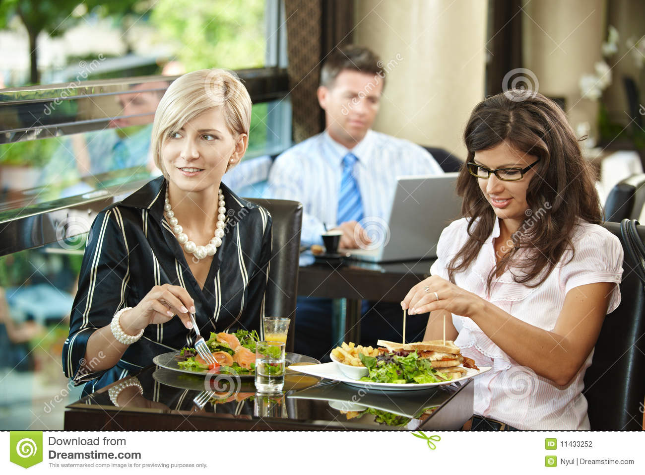 Young Women Sitting At Table Eating Sandwich And Salad In Restaurant    
