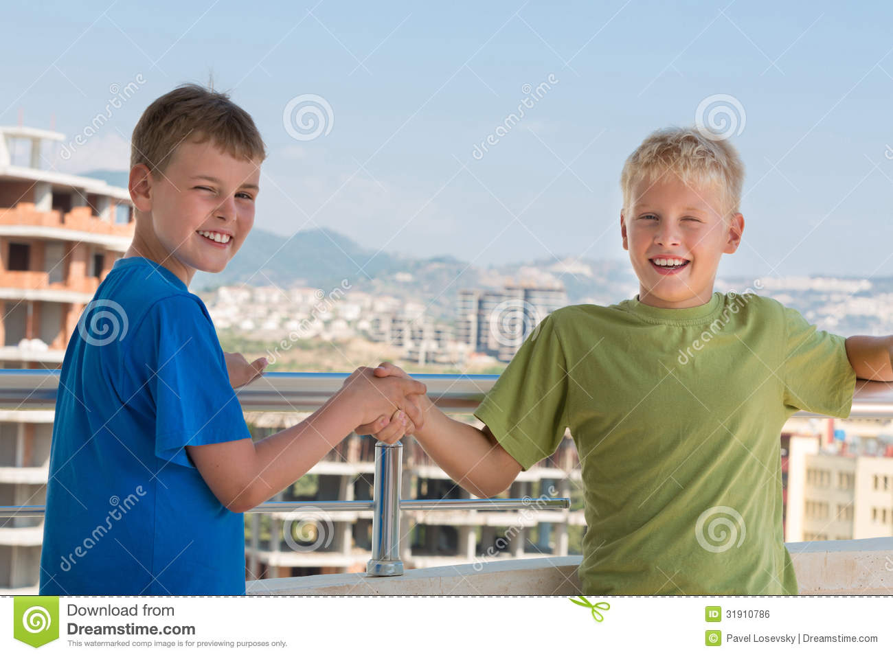Two Smiling Boys In Colored T Shirts Are Shake Hands On The Background    