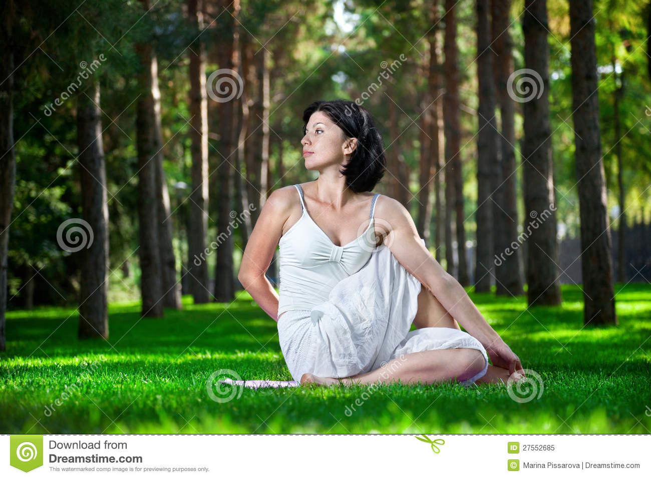Yoga Twisting Pose By Woman In White Costume On Green Grass In The