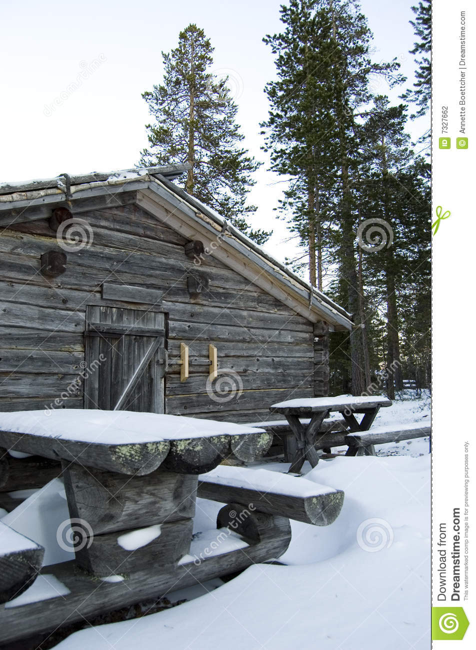 Wooden Log Cabin With Snow Covered Rustic Benches And Tables In The