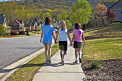 Three Young Girls Going Up A Sidewalk In A Neighborhood Holding Hands